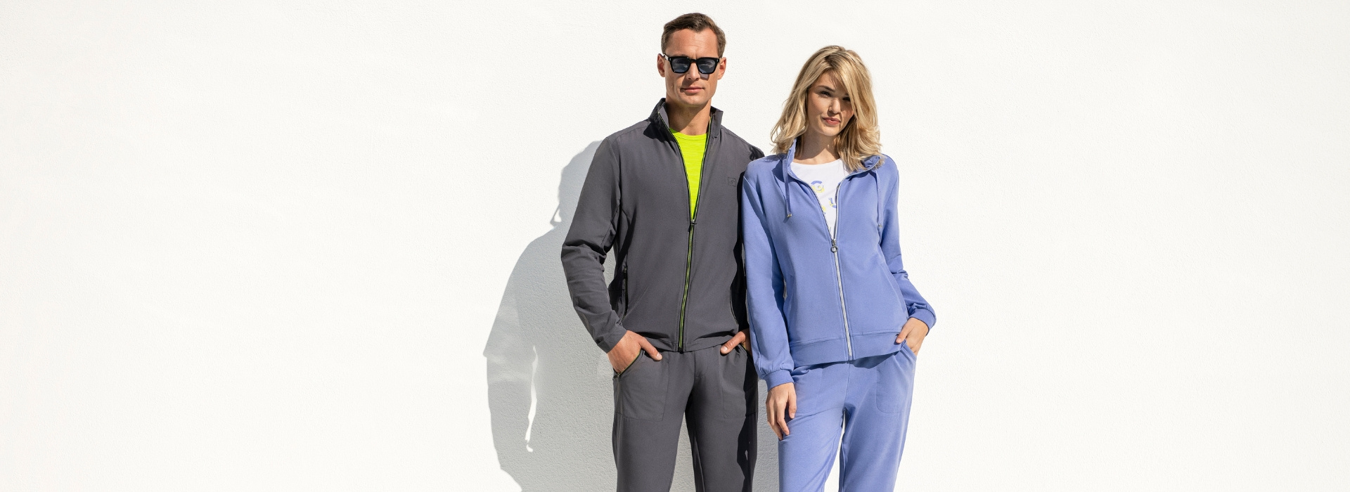 Mann und Frau stehen vor einem Pool und tragen Artikel der Marke JOY sportswear.